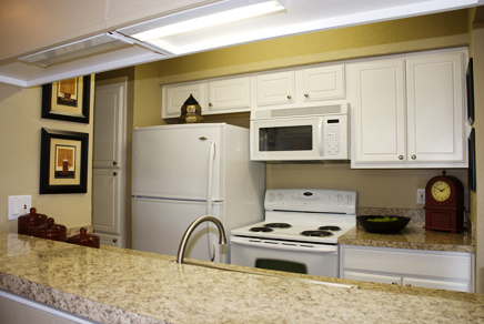 After: View of pass-through kitchen counter bar featuring granite laminate resurfacing looking to refinished and repainted cabinetry and pantry refaced with distinctive raised panel doors and complementary brushed nickel knobs. Stove counter displays new granite style countertop.