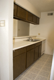 Before: Uninviting, dated dreary brown cabinetry with standard almond-colored countertops in galley-style kitchen were rejuvenated with an invigorating update featuring distinctive granite laminate countertops and refaced sink and overhead cabinets with raised panel doors and brushed nickel hardware.