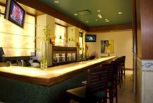 Custom built hotel Bar features wood framework, bar surface of translucent glass, and mosaic tile decorative facing. Shelving and backlit bottle display are framed with Bonier's custom millwork.