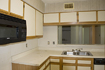Before: Cabinets and counters in dated light oak finish with white laminate panel faces and matching white countertops.
