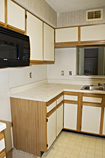 Before: Dated and worn yellow oak cabinets with white laminate door facings and exposed hinges and white laminate countertops.